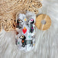 A clear glass can-shaped tumbler with a bamboo lid and straw, decorated with colorful dachshund illustrations in a Day of the Dead style, resting on a white faux fur surface next to a woven mat.