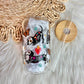 A clear glass tumbler with a bamboo lid and clear straw, decorated with colorful dachshund illustrations and paw prints, displayed on a white faux fur surface next to a woven mat.